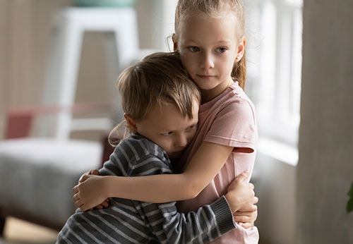 A concerned older sister comforts her younger brother with a warm hug.